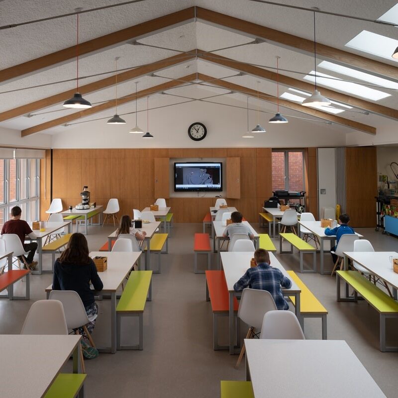 Students social distancing in a classroom with a digital display in the front.